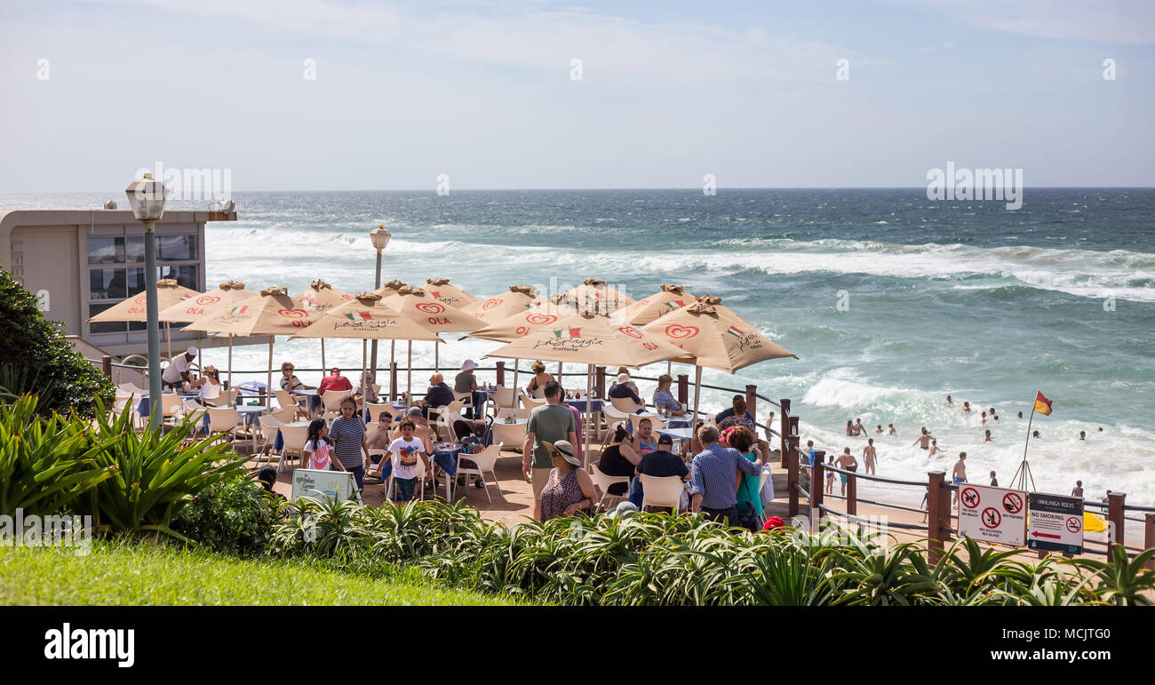 Durban, Südafrika, April 9 - 2018: Cafe entlang am Strand mit Sonnenschirmen. Die Badegäste können in das Meer im Hintergrund gesehen werden. Stockfoto