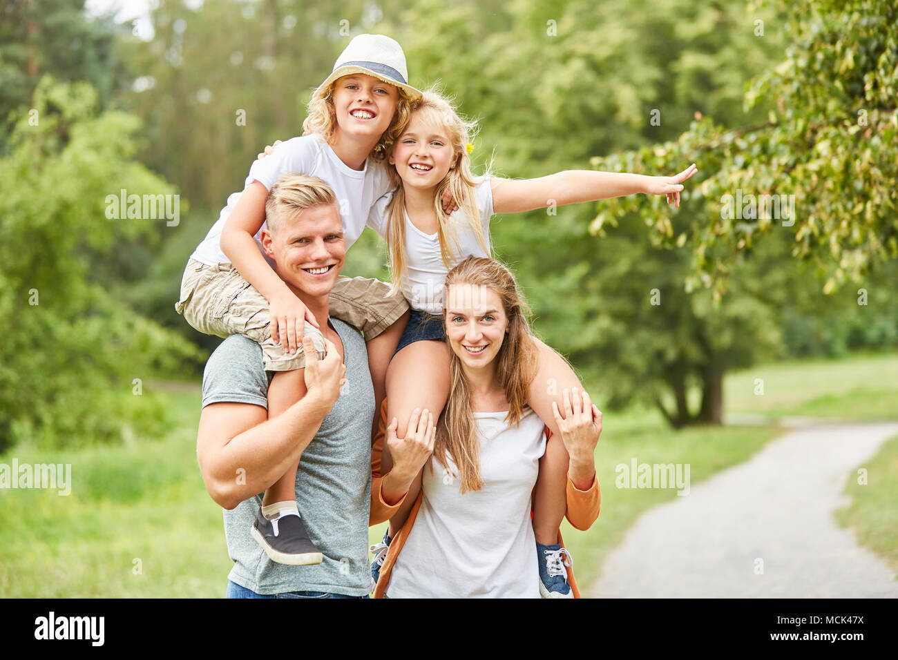 Glückliche Kinder reiten Huckepack auf ihre Eltern auf einer Wanderung Stockfoto