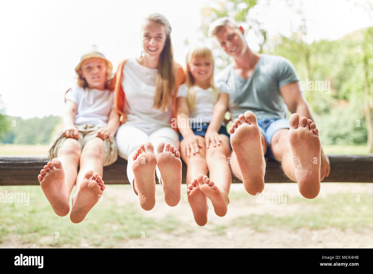 Glückliche Familie und Kinder sitzen barfuß auf einer Parkbank im Sommer Stockfoto
