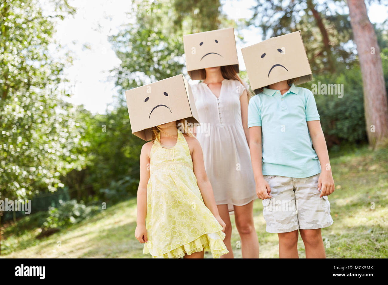 Anonyme Familie ist versteckt unter Kartons mit einer Trauer Gesicht in einem Garten Stockfoto