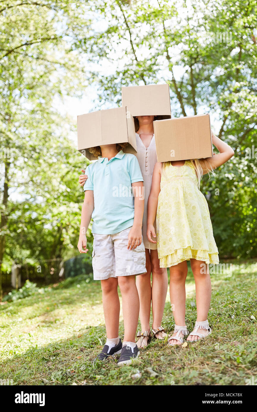 Mutter und Kinder sind anonym unter Pappkartons im Garten Stockfoto