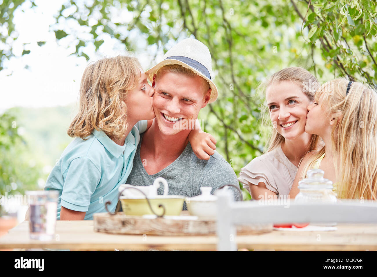 Kinder ihren Eltern Küssen auf die Wange im Garten am Frühstückstisch Stockfoto