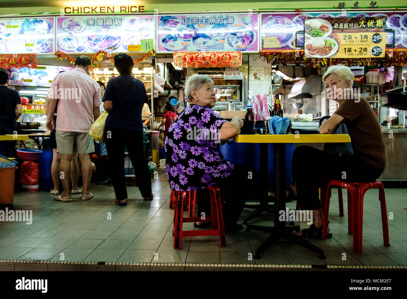 Singapur - Januar 29, 2014: Zwei alte Frauen sitzen auf einem Tisch in der Hawker Center, wo Singaporean Menschen die Vielfalt der preiswertes Essen genießen. Stockfoto