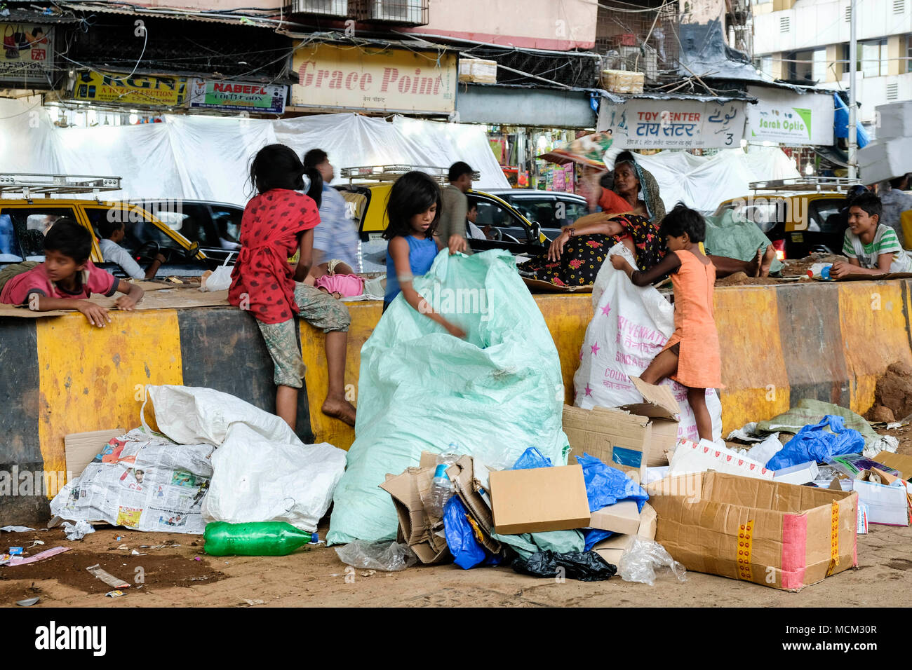 Straßenkinder arbeiten beim Sammeln von Pappe und Müll in der Innenstadt von Mumbai. Viel Verkehr hinter dem Hotel, Schild mit der Aufschrift „Grace Point“, Mumbai, Indien Stockfoto