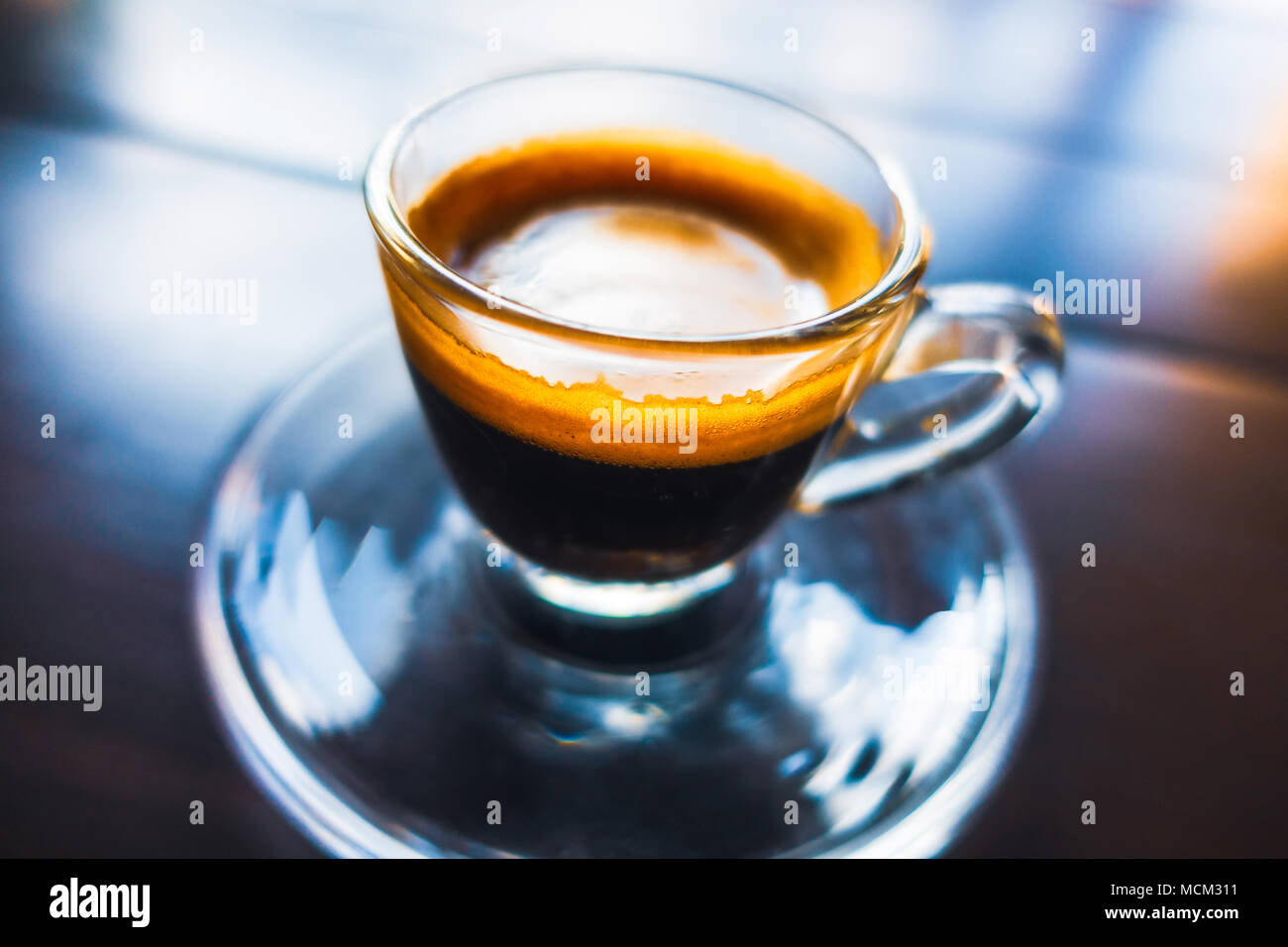 Espresso in Glas Schale auf Holztisch, bunte Reflexionen und flache Tiefenschärfe. Stockfoto