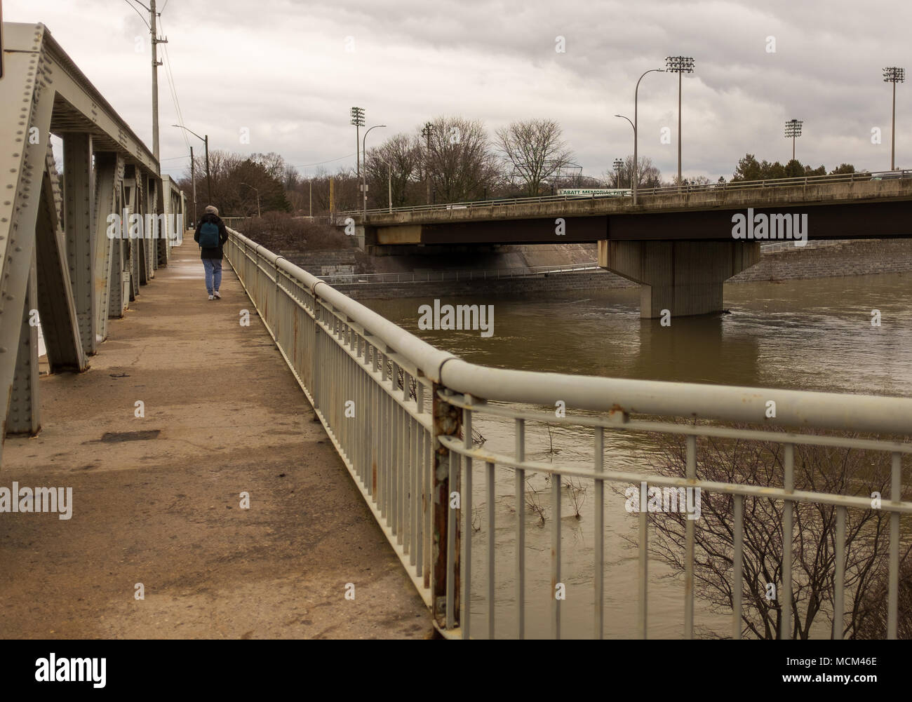 Eine Frau geht auf dem Gehweg einer Brücke an der Themse. Ungewöhnlich kühle Wetter und zwei Tage Regen, Schnee und Eisregen Stockfoto