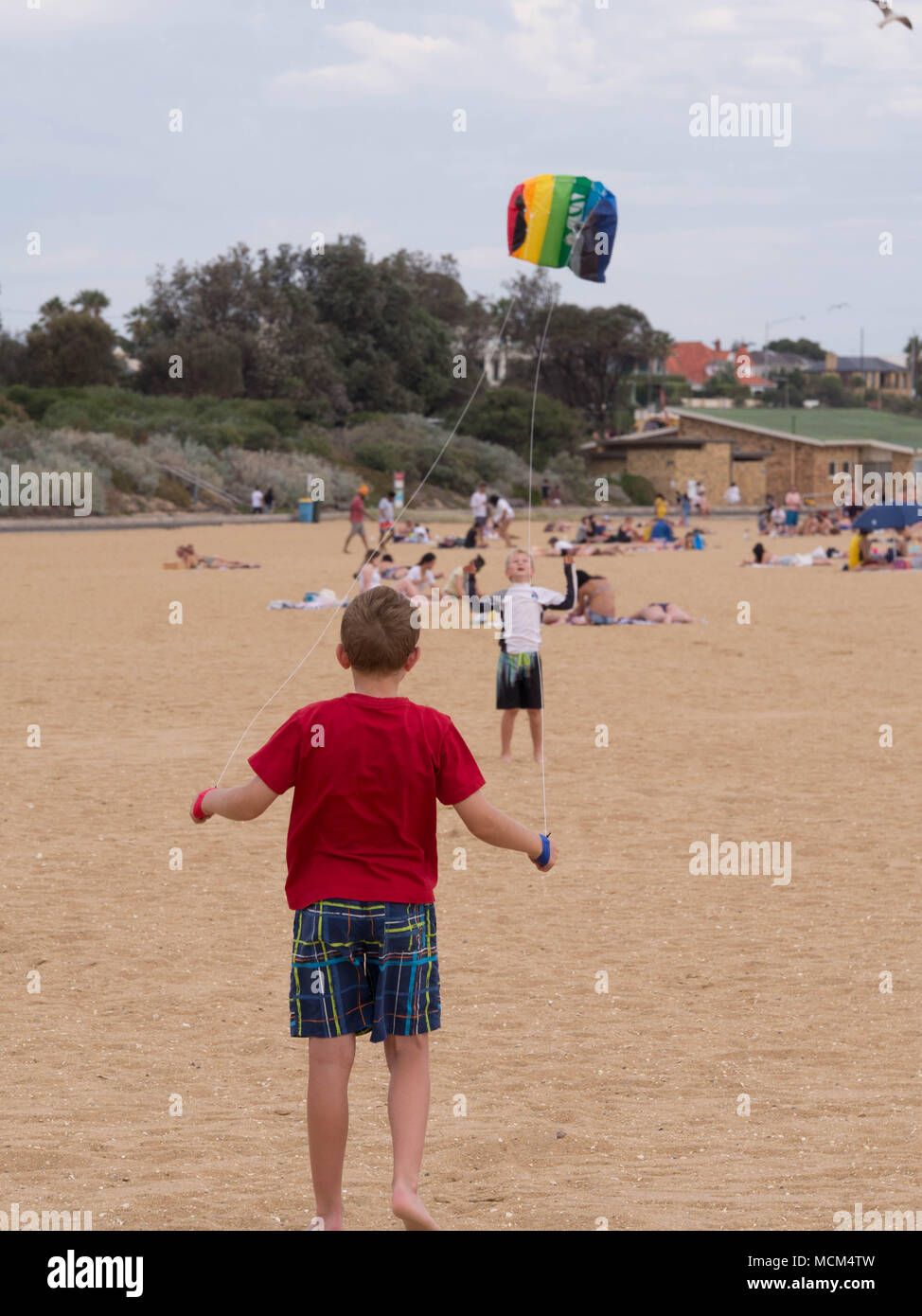 Zwei kleine Jungen im Vordergrund Holding kite Kontrollen im Abstand halten bunte Drachen und den Start in die Luft an einem wunderschönen Strand. Stockfoto