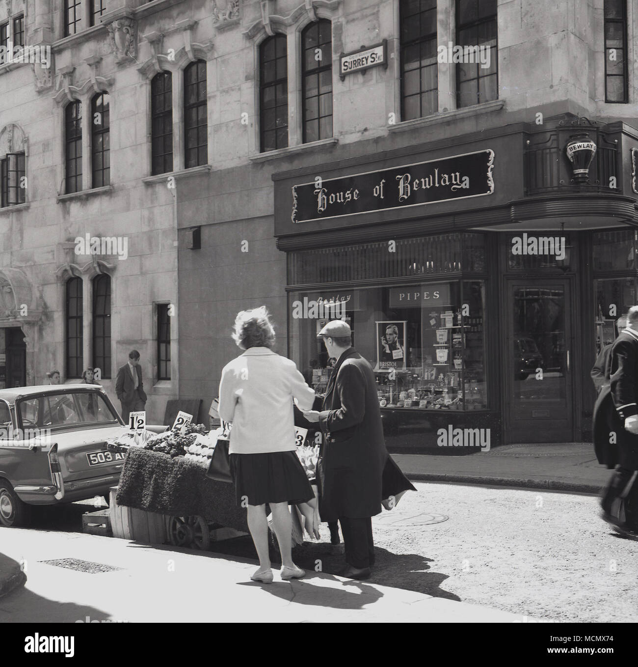 1960, historische, London, eine Straße Obst Anbieter mit einer weiblichen Kunden. Hinter Ihnen ist ein 'Haus der Bewlay" speichern, ein Einzelhändler der Pfeifen und Tabak zunächst in London im Jahre 1780, der in den Strand von Thomas Bewlay. Es wird an dieser Stelle über 50 Stores in London und die gleiche Anzahl in den Städten in den Rest von Großbritannien entfernt hatte. Das Rauchen einer Pfeife war eine beliebte Freizeitbeschäftigung in dieser Ära. Stockfoto 1960, historische, London, eine Straße Obst Anbieter mit einer weiblichen Kunden. Hinter Ihnen ist ein 'Haus der Bewlay" speichern, ein Einzelhändler der Pfeifen und Tabak zunächst in London im Jahre 1780, der in den Strand von Thomas Bewlay. Es wird an dieser Stelle über 50 Stores in London und die gleiche Anzahl in den Städten in den Rest von Großbritannien entfernt hatte. Das Rauchen einer Pfeife war eine beliebte Freizeitbeschäftigung in dieser Ära. Stockfoto