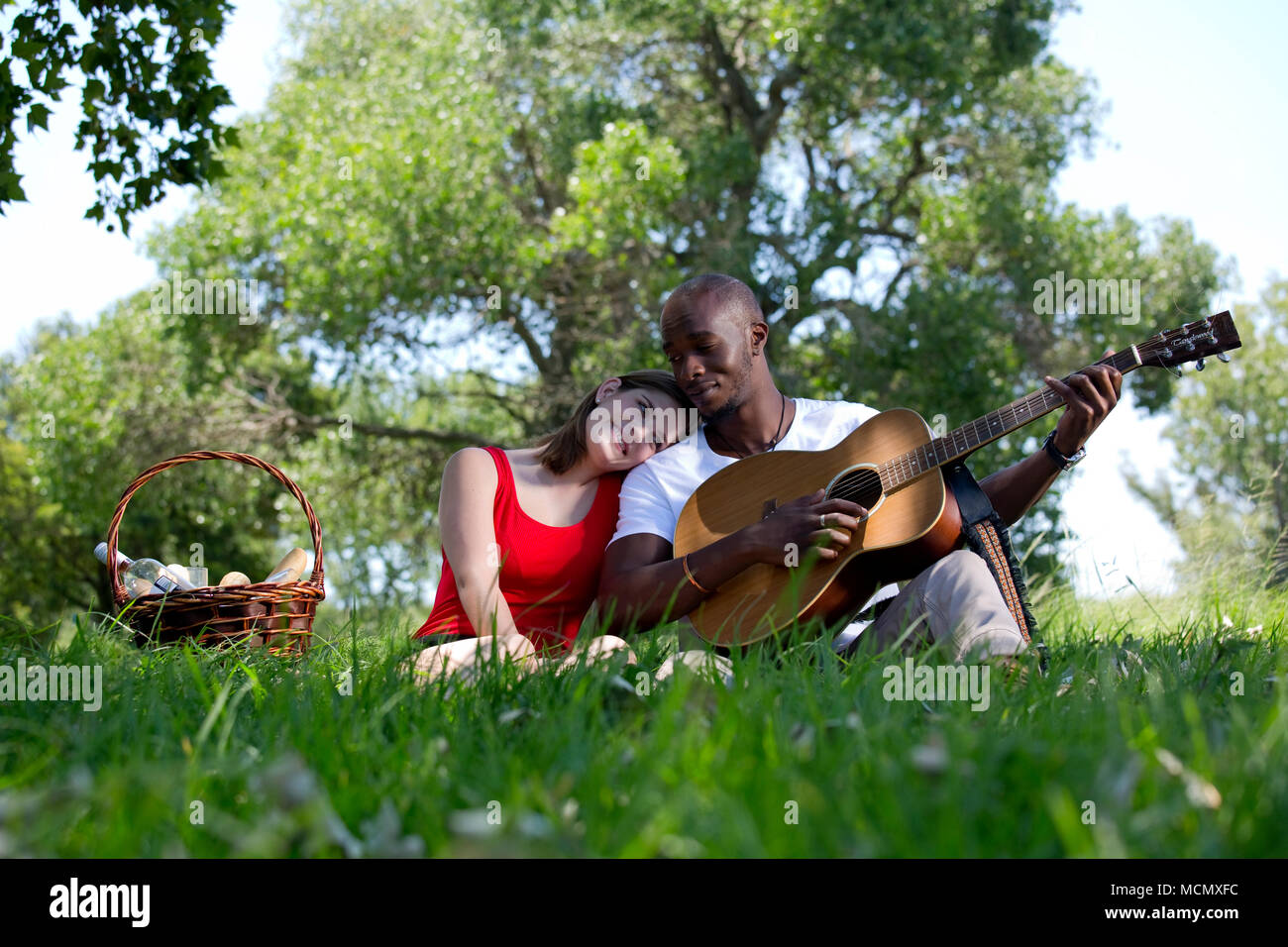 Mann spielt Gitarre für eine Frau in einem Park Stockfoto