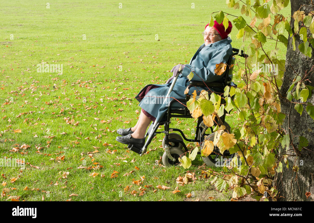 90 Jahre alte Frau im Rollstuhl genießen Sie den Sonnenschein in den öffentlichen Park. England. Großbritannien Stockfoto