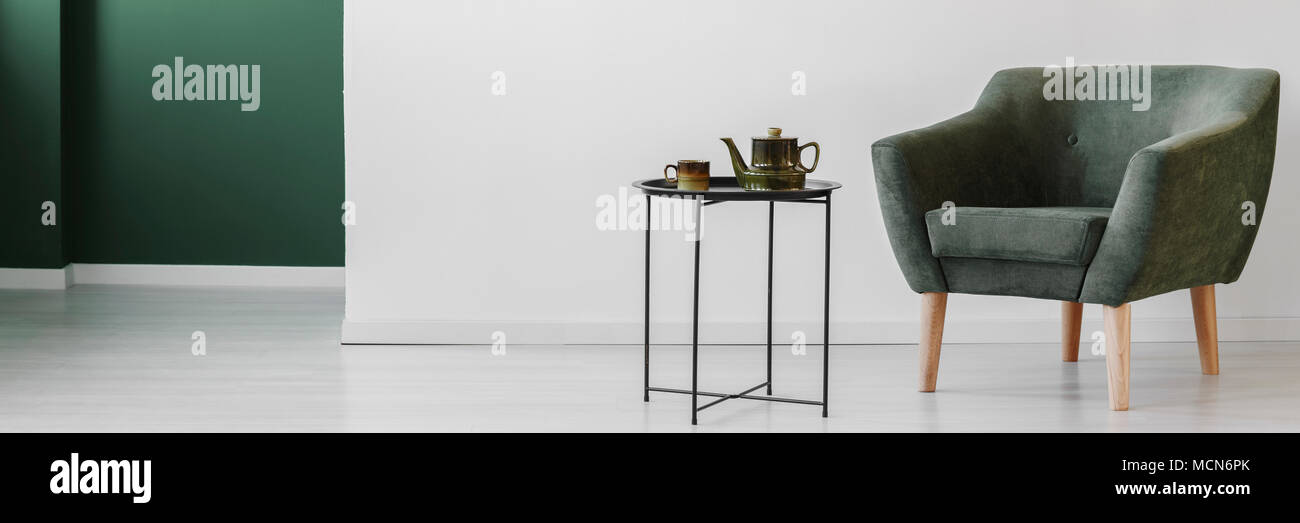 Grau Sessel neben Tabelle mit Wasserkocher gegen weiße Wand in einfachen Wohnzimmer Innenraum Stockfoto