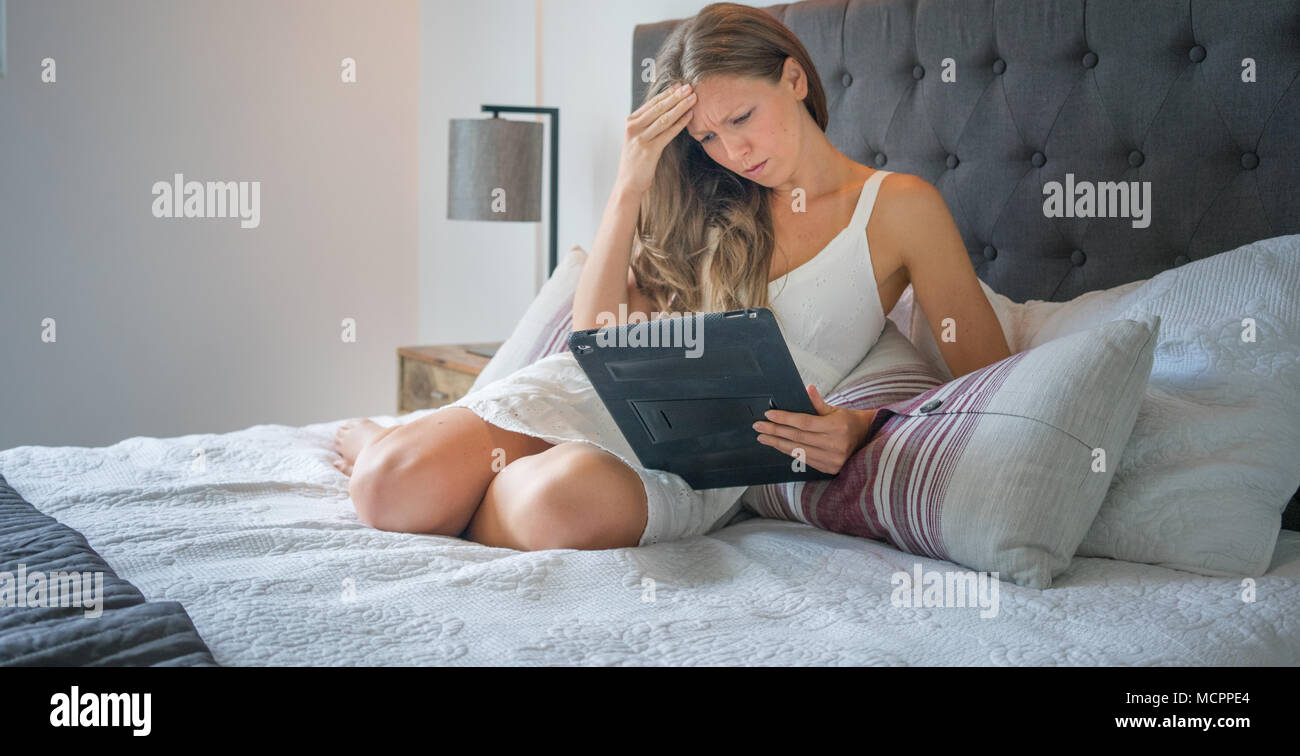 Traurige junge Frau in Nachtwäsche mit digitalen Tablet beim liegen auf dem Bett Stockfoto