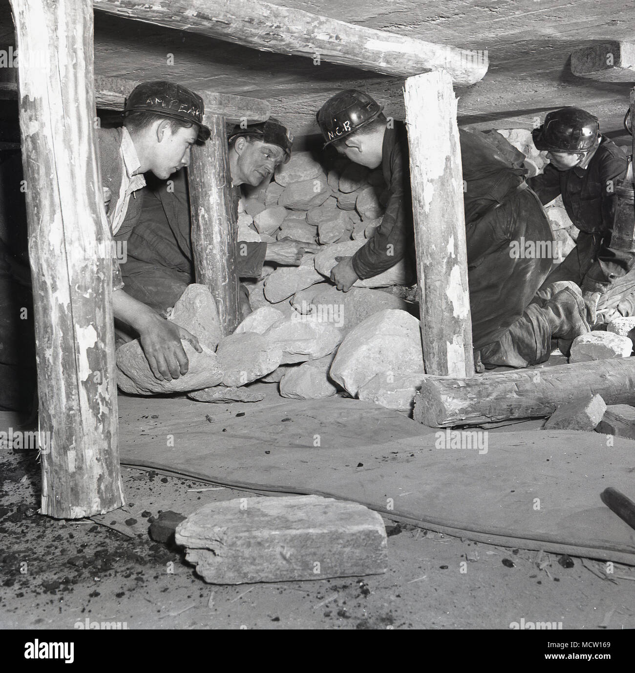 1950er Jahre, historische, Bergbau Studenten gezeigt wird, wie Felsen sicher in einem geschlossenen u-Zeche entfernen, mit seinem Dach durch Holzbalken auf hölzernen Requisiten unterstützt. England, UK. in Großbritannien, Bergbau war immer noch ein wichtiger Wirtschaftszweig mit über 500 Gruben in der Existenz und der Regierung des Tages aktiv ermutigt junge Menschen Bergbau Kenntnisse und Fähigkeiten zu erwerben und die Industrie zu geben. Stockfoto