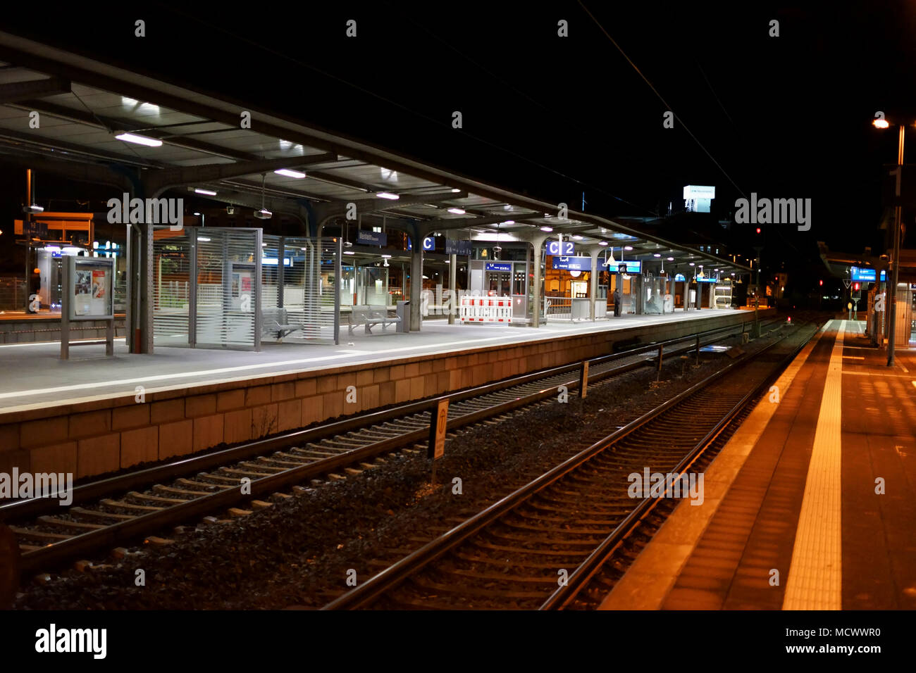 Die Plattform der Weinheimer Bahnhof bei Nacht mit Sitzen, Schienen und Glas. Stockfoto