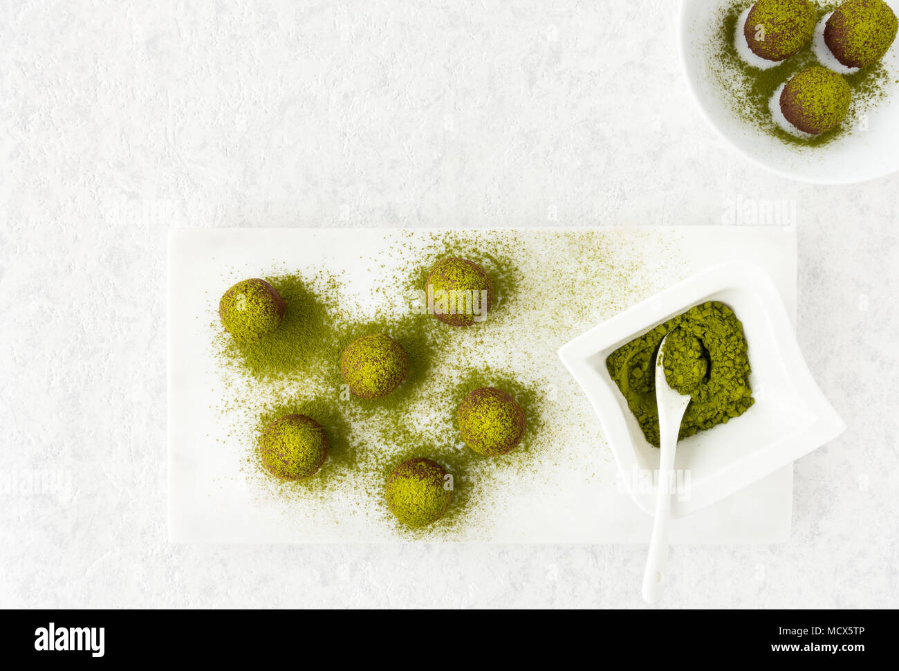 Blick von oben auf die Matcha Schokolade Trüffel und eine kleine Schüssel mit grünem Matcha Pulver gefüllt auf weißem Marmor Schneidebrett. Stockfoto