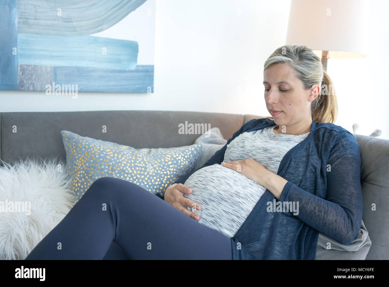Frau berühren Ihren schwangeren Bauch, während ein Nickerchen auf dem Sofa Stockfoto