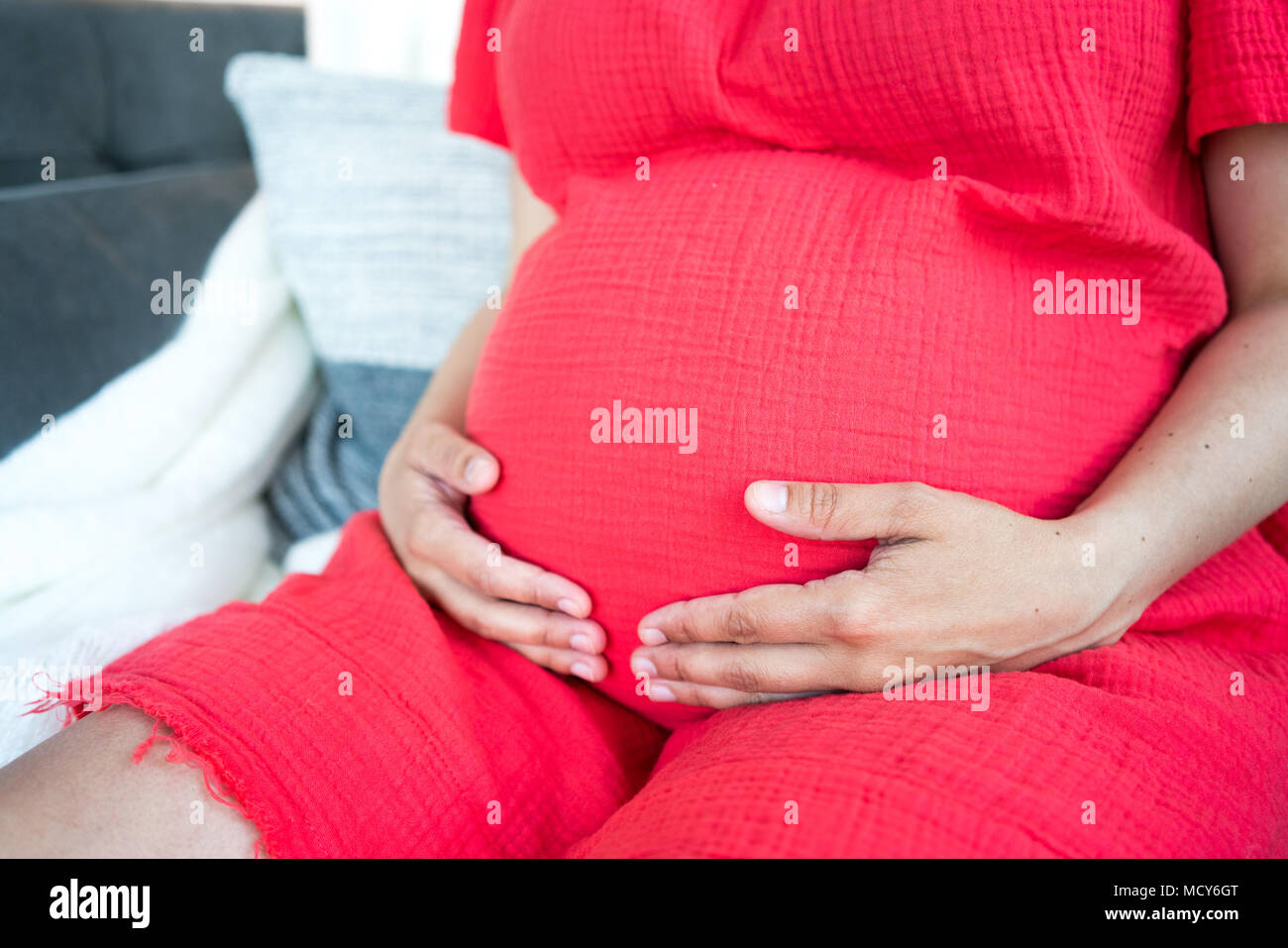 Mittelteil der schwangeren Frau sitzt auf der Couch und hält ihre schwangeren Bauch Stockfoto