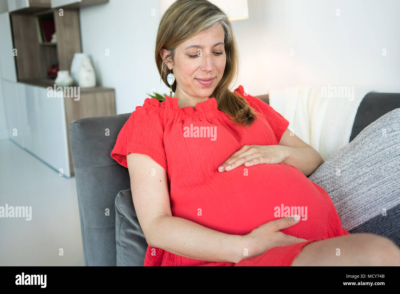 Schwangere Frau lehnte sich auf dem Sofa und hielt ihre schwangeren Bauch Stockfoto