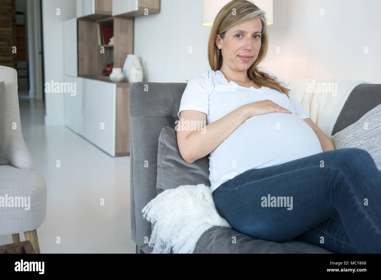 Schwangere Frau lehnte sich auf Sofa und berühren ihre schwangeren Bauch Stockfoto