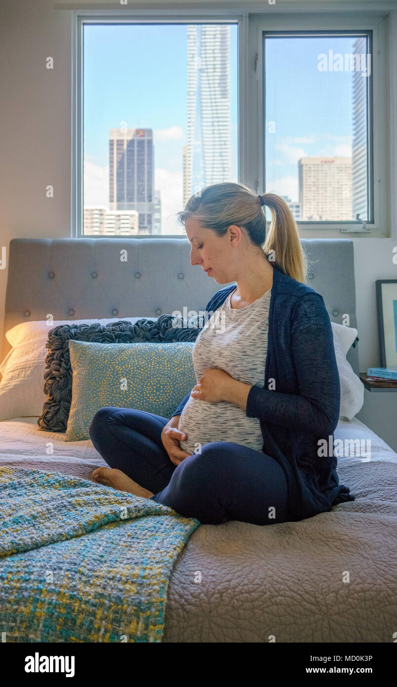 Frau sitzt auf dem Bett und ihre schwangeren Bauch berühren. Stockfoto