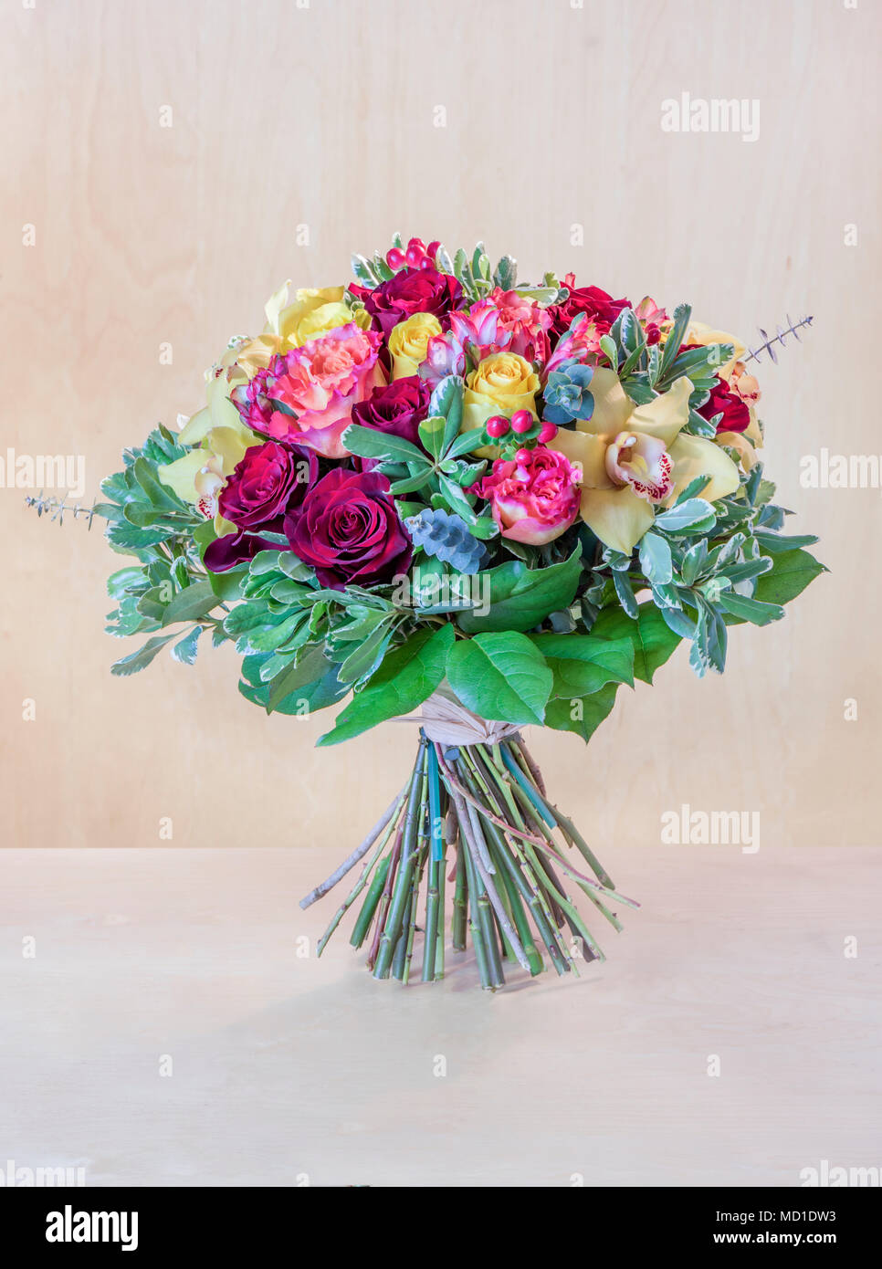 Schönen Blumenstrauß, bunte Rosen mit grünen Blättern steht auf einem hellgrauen Tabelle, braunen Hintergrund mit einer Baumstruktur Stockfoto