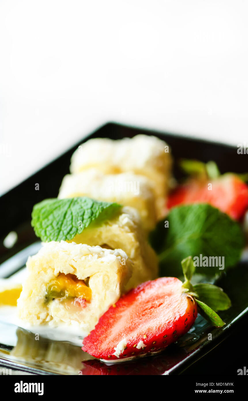 Weiße Brötchen mit Kiwi, Pfirsiche, Erdbeeren, Minze. Serverd mit Mandel Pfirsich- und Schokolade Saucen auf schwarzem Teller. Süße Nachspeise für Mädchen, Frau, Stockfoto