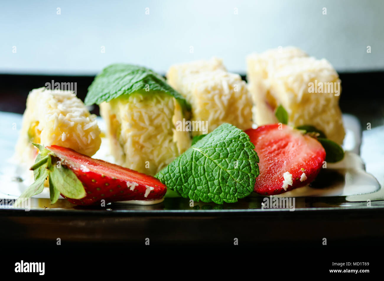 Weiße Brötchen mit Kiwi, Pfirsiche, Erdbeeren, Minze. Serverd mit Mandel Pfirsich- und Schokolade Soßen auf schwarze Platte Stockfoto