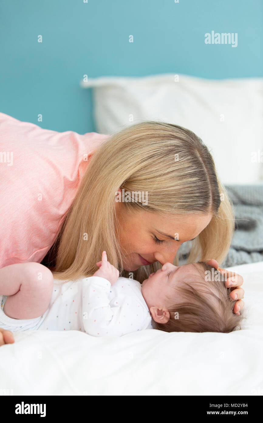 Jung, schön und blond Mutter mit rosa Shirt ist Kuscheln mit Ihrem Baby im Bett Stockfoto