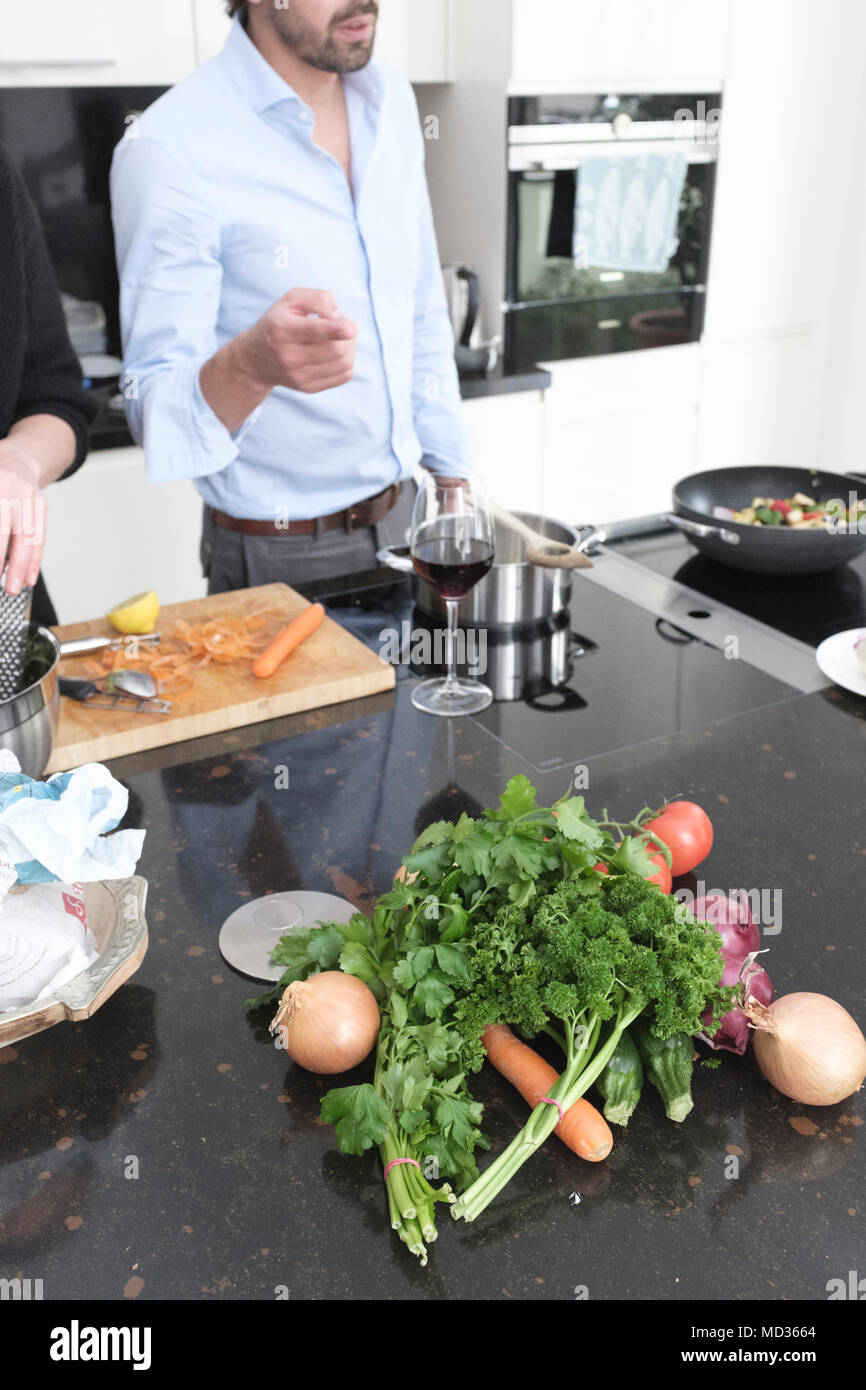 Selektiver Fokus - frische Kräuter und Gemüse auf dem Küchentisch. Gruppe von Freunden zusammen kochen beim Lachen und sich zu amüsieren. Stockfoto
