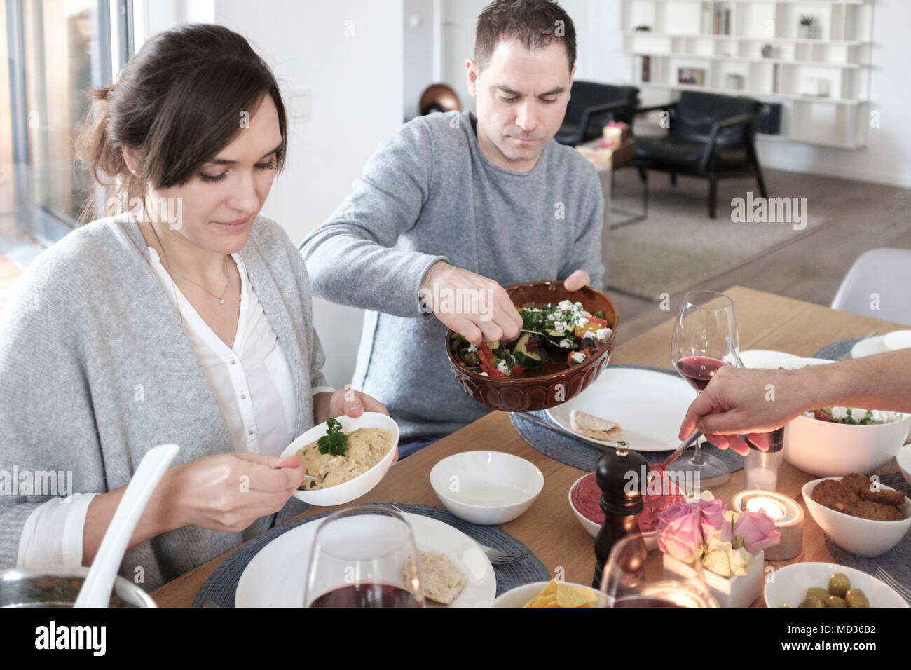 Gruppe von Freunden beiläufig Snacking auf eine Auswahl von Lebensmitteln beim Lachen und sich zu amüsieren. Mit gebratenem Gemüse-selektiven Fokus Stockfoto