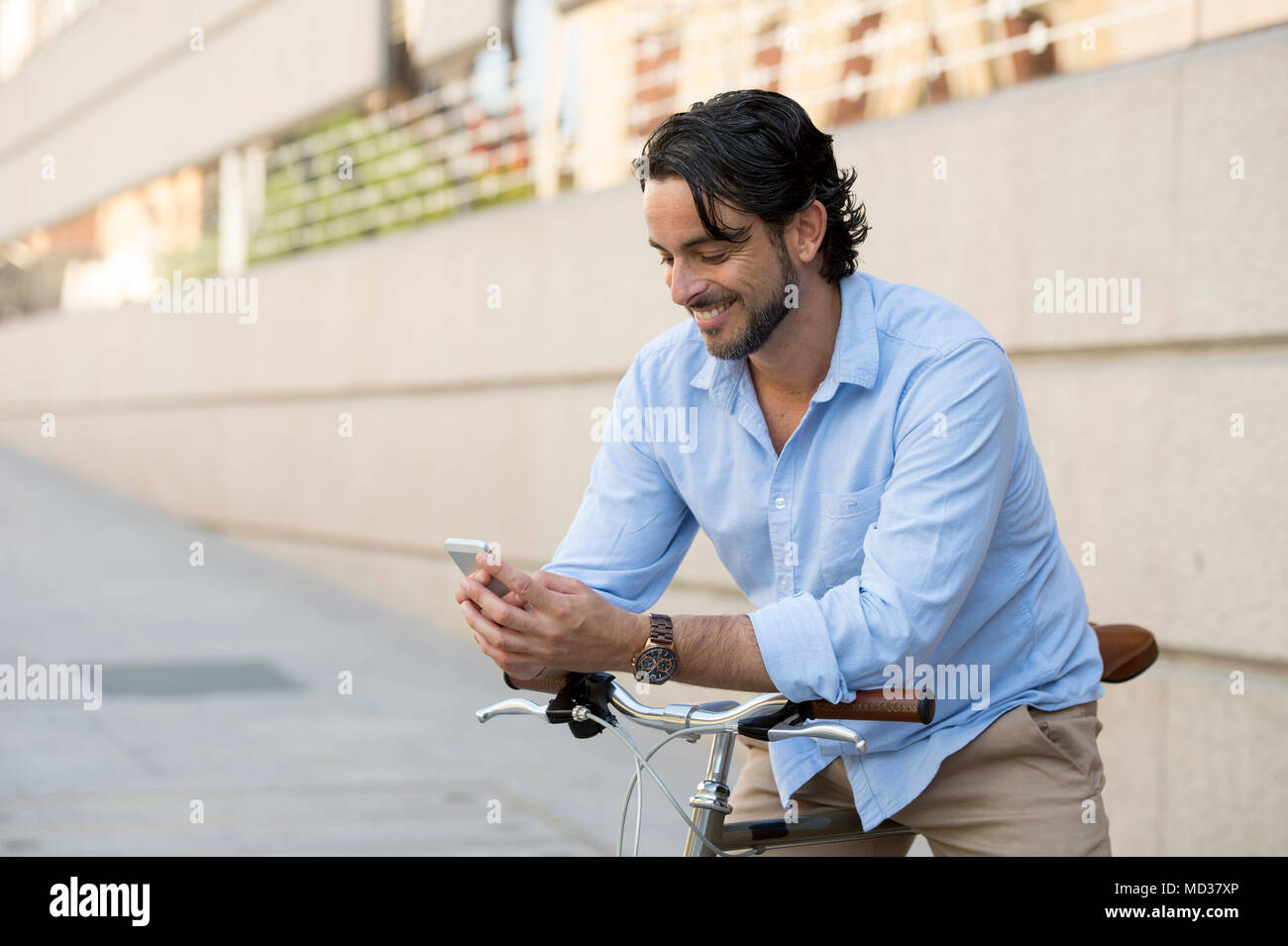 Junge glücklich attraktive Hispanic Mann in ungezwungener trendige Kleidung lächelt fröhlich mit Handy auf vintage Coole Retro Fahrrad in moderner, stilvoller lifes Stockfoto