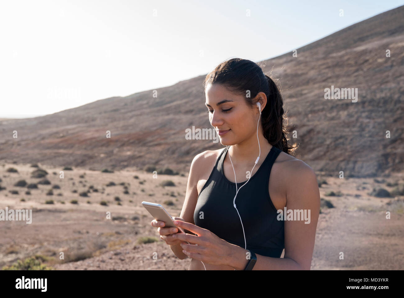 Junge weibliche Läufer an Smartphone in ariden Landschaft suchen, Las Palmas, Kanarische Inseln, Spanien Stockfoto