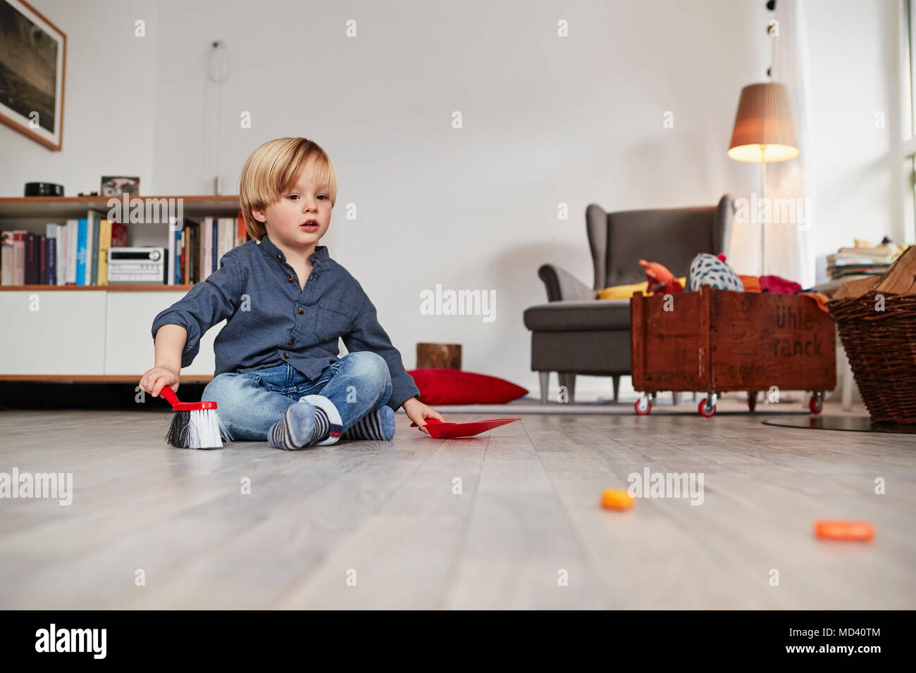 Junge Junge sitzt auf dem Boden, holding Spielzeug Handfeger und Kehrblech Stockfoto