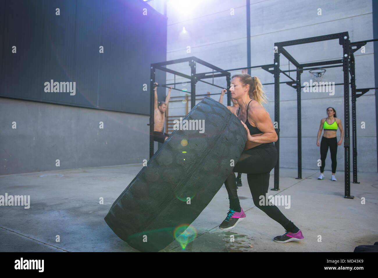 Vier Leute trainieren im Fitnessraum, Frau im Vordergrund heben Reifen Stockfoto