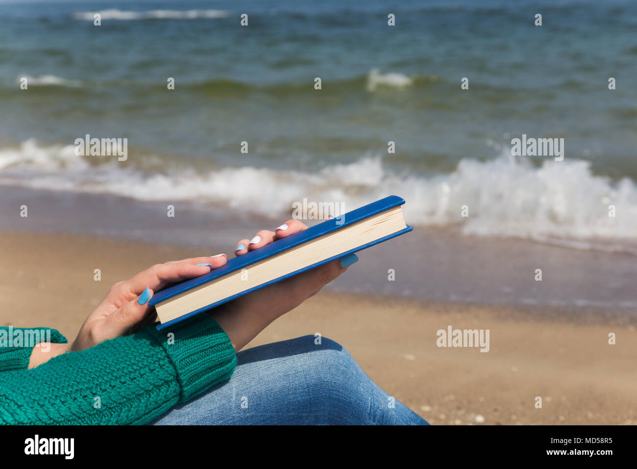 Detailansicht der zwei weiße weibliche Hände, die dicken blauen Buch. Frau liest am Meer Strand an sonnigen Frühling, Herbst oder kühlen Sommer Tag während Beach hol Stockfoto