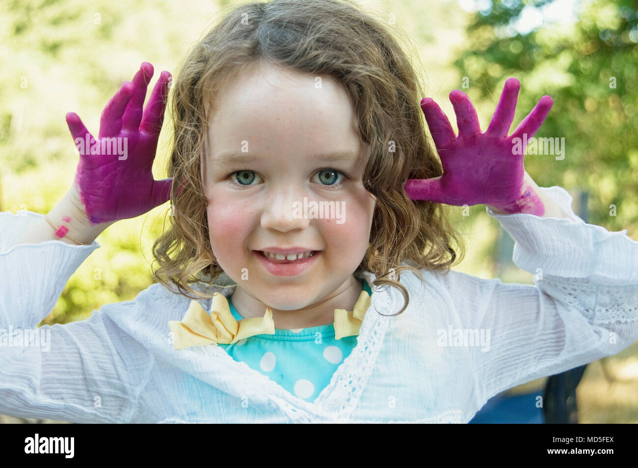 Ein junges Mädchen (3-5 Jahre) mit dem lockigen Haar und fingerpaint auf ihre Hände. Stockfoto