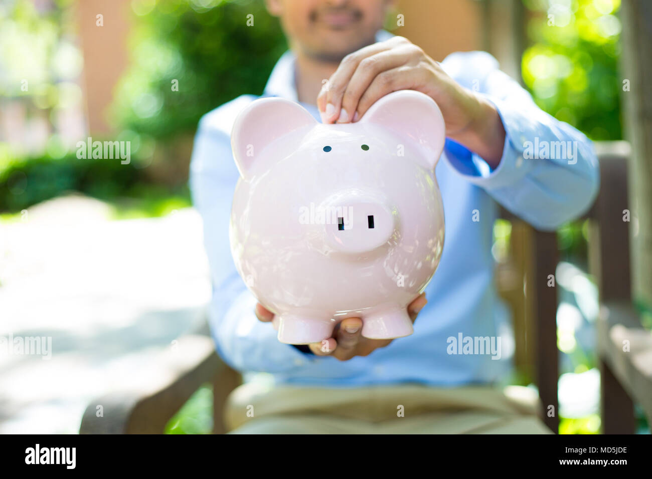 Closeup Porträt, junge Geschäftsmann Münzen im Sparschwein, isoliert im Freien Bäume Hintergrund. Smart weisen Währung finanzielle Investitionen Reichtum Stockfoto