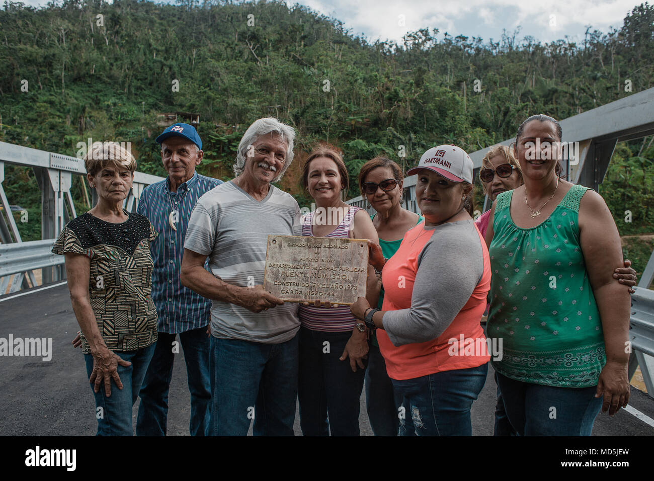 Utuado, Puerto Rico. März 13, 2018 -- Überlebenden Posieren vor der neuen Brücke und der Widmung Plakette der vorherigen zeigen. Diese Menschen unter vielen anderen Familien wurden durch den Zusammenbruch der früheren Brücke nach Hurrikan María durch die Insel am 20. September 2017 Rissen betroffen. Heute, dank der Bemühungen der staatlichen, lokalen und föderalen Agenturen, hat die Gemeinschaft eine neue Brücke. Die FEMA/Eduardo Martínez Stockfoto