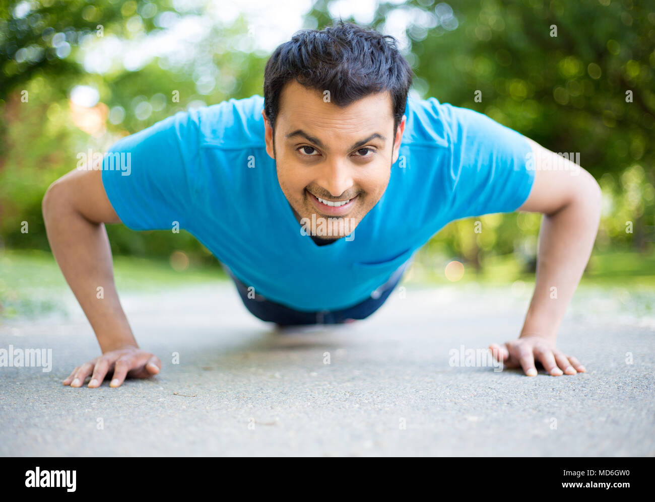 Closeup Porträt, junge, gesunde und gut aussehender Mann Durchführung pushup draußen auf der Straße in den Park, vereinzelte Bäume und Himmel Hintergrund. Stockfoto