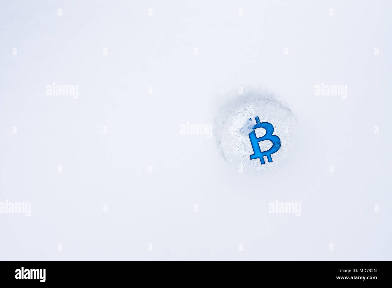 Eine Münze von Bitcoin crypto Währung in den Schnee geworfen. Silber bitcoin mit blauen B im Schnee allein. Stockfoto