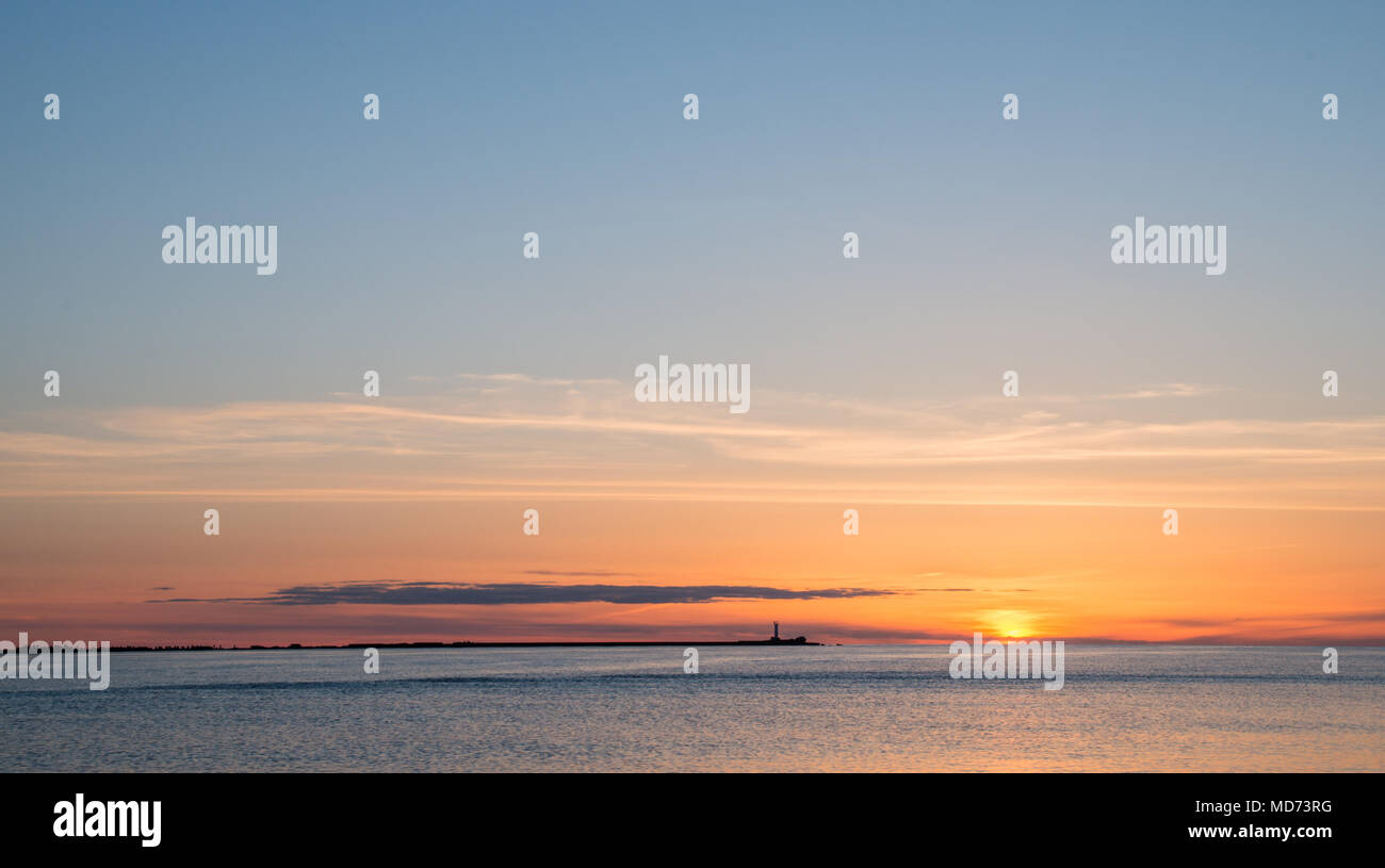 Die Silhouette eines entfernten Mole mit ruhigen Meer und die untergehende Sonne in orange Himmel. Stockfoto