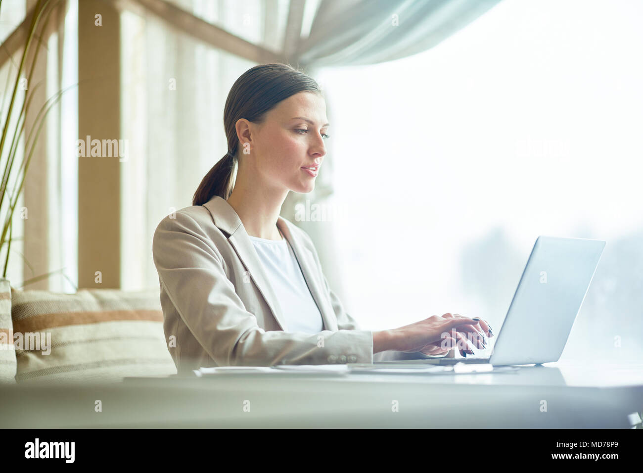 Junge elegante Kaukasischen Geschäftsfrau Tippen auf Laptop am Tisch im Restaurant sitzen und warten auf das Mittagessen Stockfoto