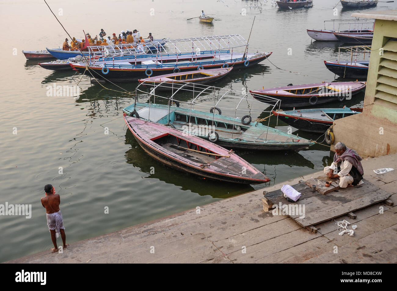 Ein Mann bereitet rituellen Opfergaben und ein anderer Mann steht nach dem Bad im Ganges an den ghats in Varanasi Stockfoto