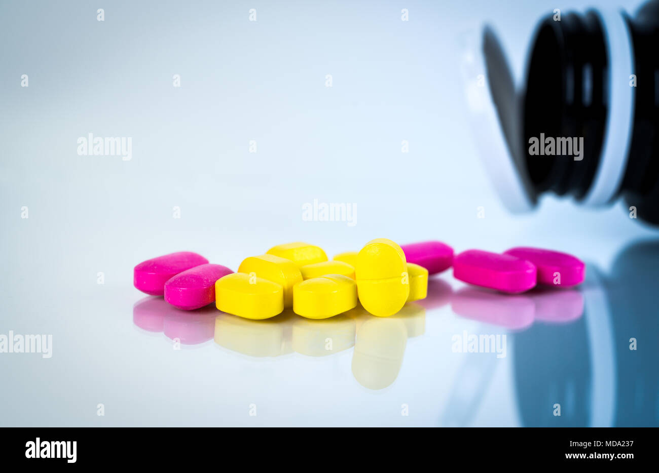 Gelb und Rosa, ovale Tablette Pillen mit Schatten auf weißem Hintergrund mit unscharfen Pillen Flasche. Leichte bis mäßige Schmerzen Management. Schmerzmittel Medizin. Stockfoto