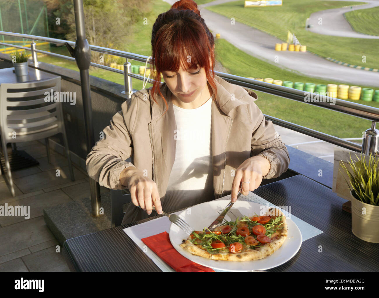 Schöne junge Frau Essen eine Pizza im Restaurant. Im Hintergrund, grünen Park mit Go-Kart-Bahn Stockfoto