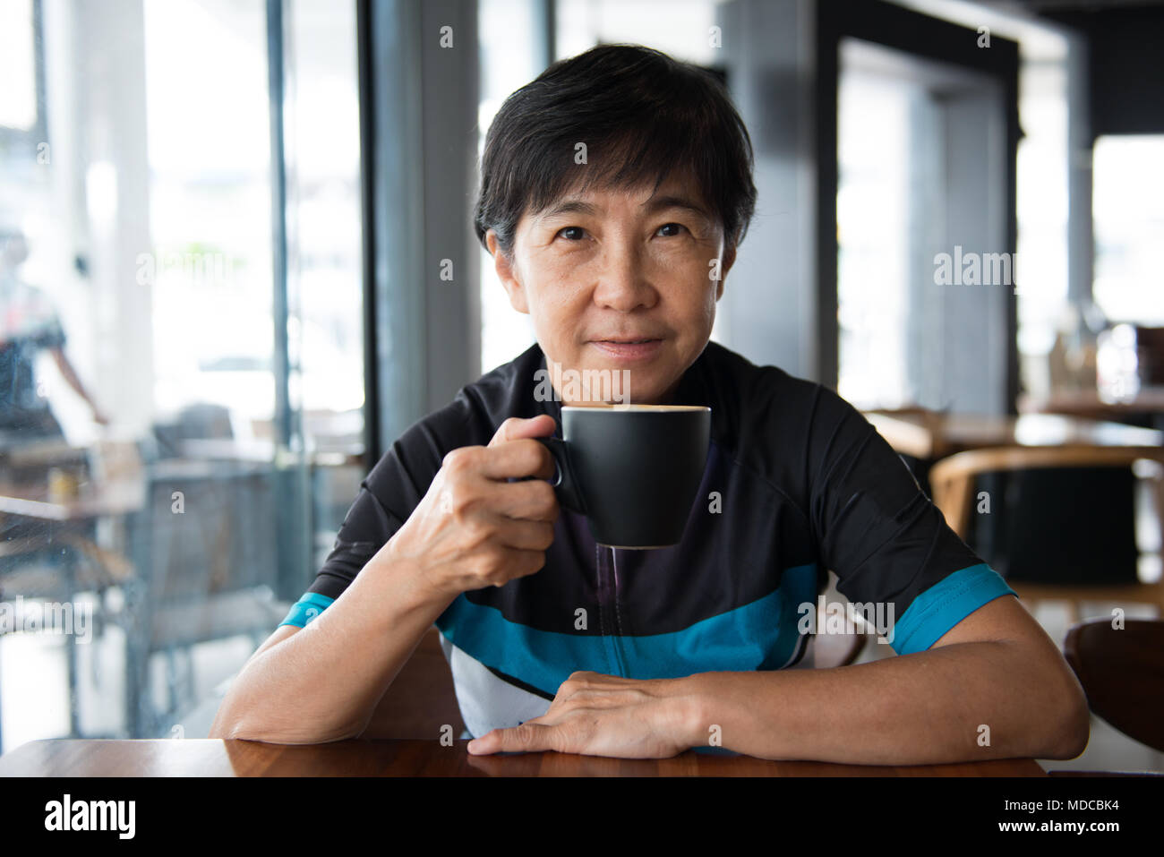 Senior asiatische Frau mit Kaffee in Trikot Stockfoto