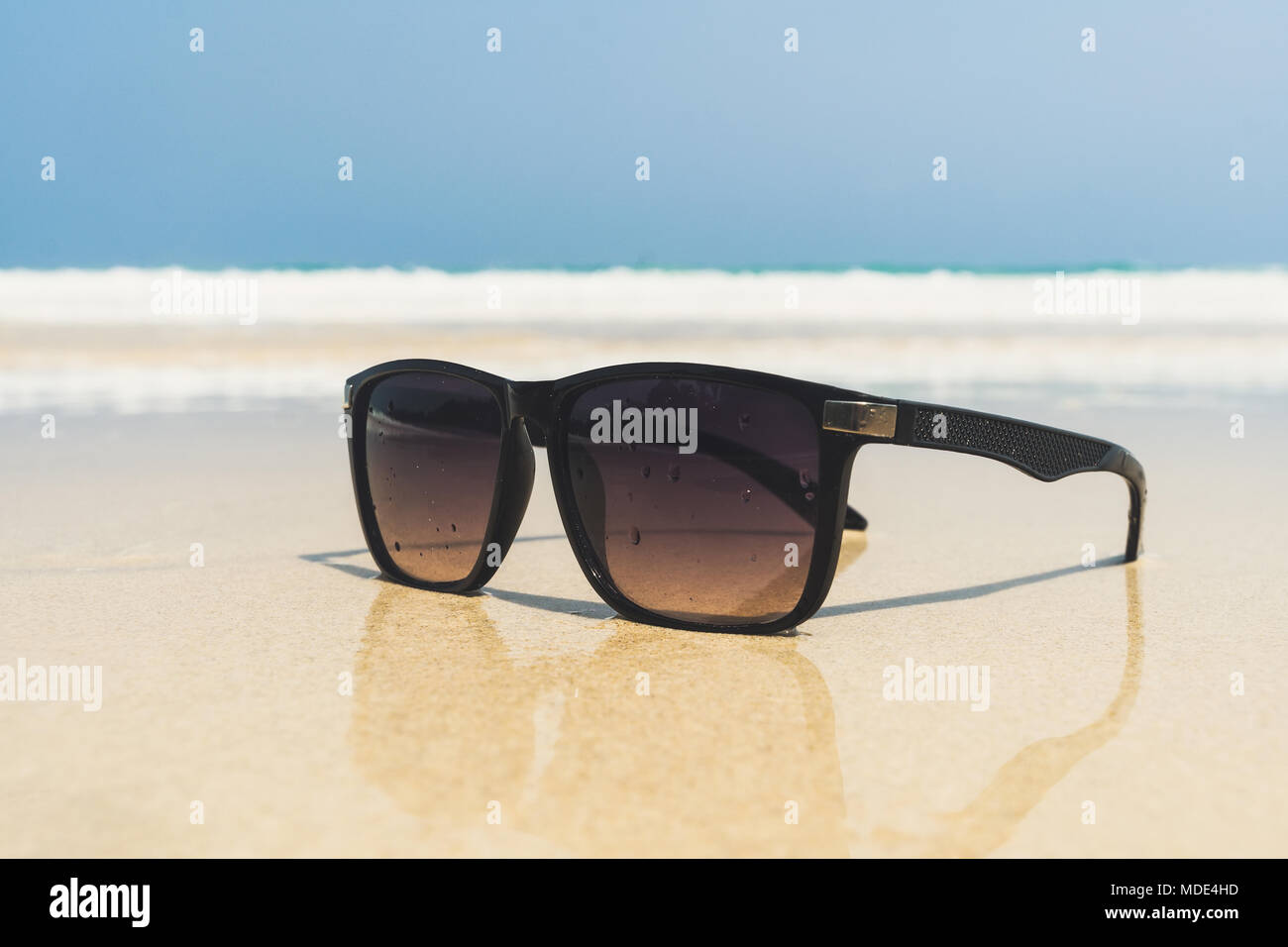 Sonnenbrille liegen auf einem Strand in der Nähe des Meeres. schwarze  Sonnenbrille auf dem Hintergrund der sea wave am Ufer eines tropischen  Insel. Sonnenbrillen sind reflecte Stockfotografie - Alamy