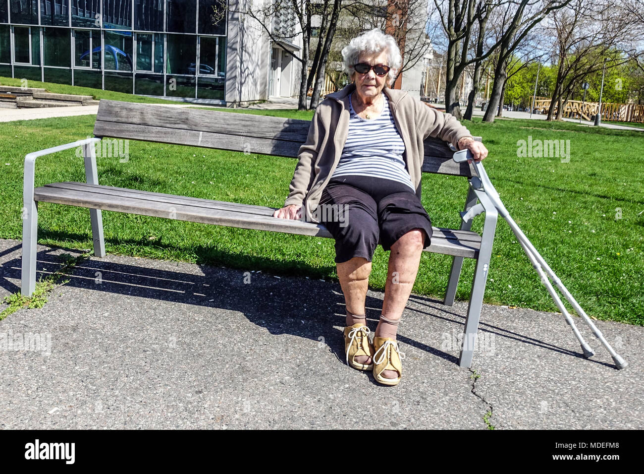 Eine ältere Dame, die auf einer Parkbank sitzt, eine alte Bank, eine Seniorin allein Stockfoto