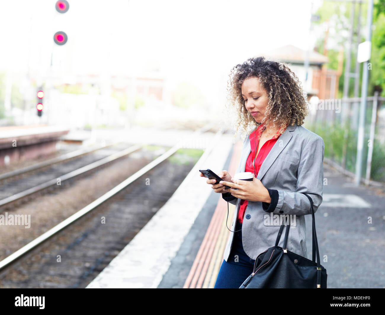 Mitte der erwachsenen Frau stehend auf Bahnsteig, Smartphone, Holding einweg Kaffeetasse Stockfoto