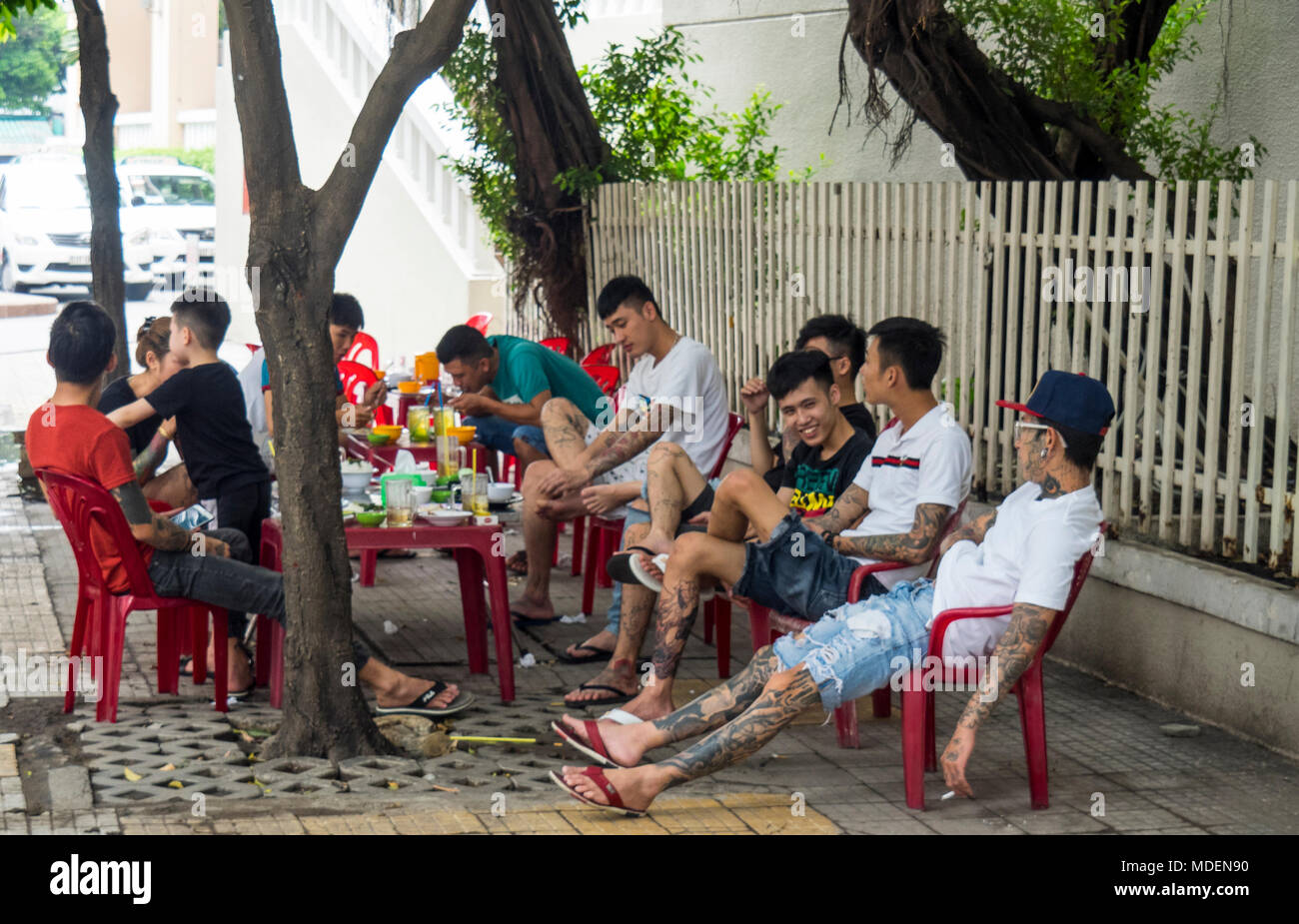Eine Gruppe von vietnamesischen Jugendlichen, meist männlichen, sitzen auf Plastikstühlen mit Mittagessen auf dem Gehweg einer Straße in Ho Chi Minh City, Vietnam. Stockfoto